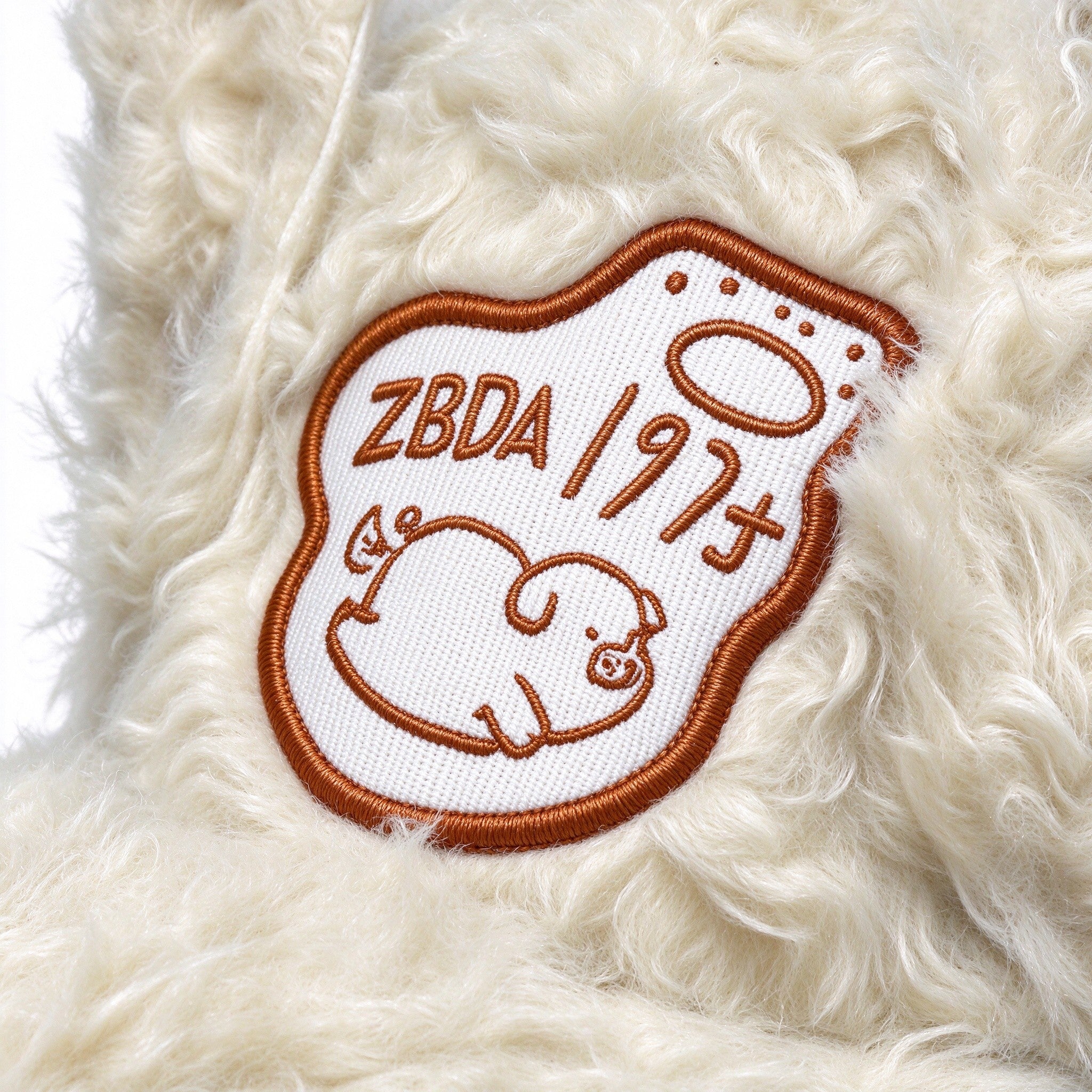 Close-up of the embroidered sleeping pig patch on the cream plush cap
