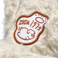 Close-up of the embroidered sleeping pig patch on the cream plush cap