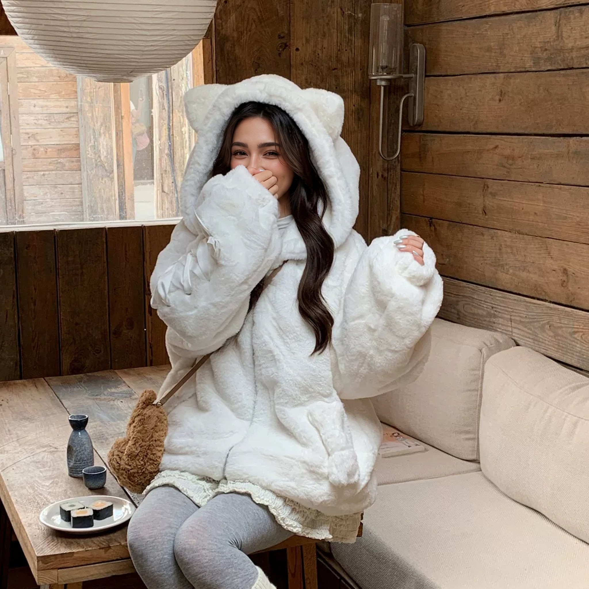 Cat Ear Hood Fluffy Zip Jacket with Ribbon Sleeves in white, worn sitting in a cafe with the hood up